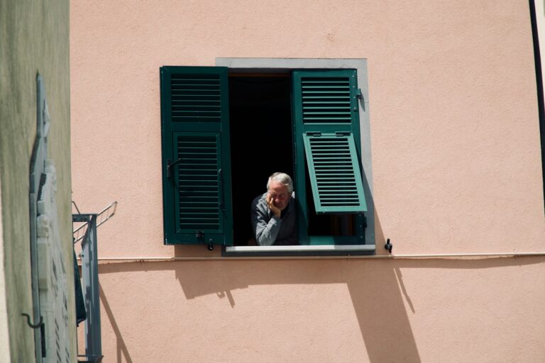 Elderly person looking out an open window in contemplation